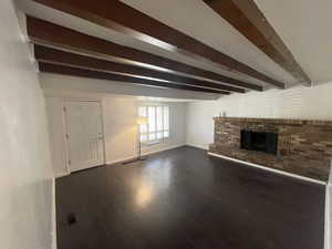 Unfurnished living room featuring a brick fireplace, dark hardwood / wood-style floors, and beam ceiling