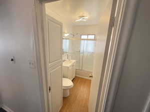 Full bathroom with toilet, combined bath / shower with glass door, vanity, and wood-type flooring