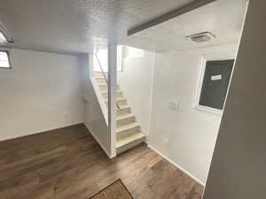 Basement with electric panel, dark wood-type flooring, and a textured ceiling