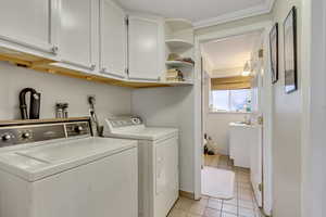 Washroom with washing machine and dryer, cabinets, light tile patterned floors, and crown molding