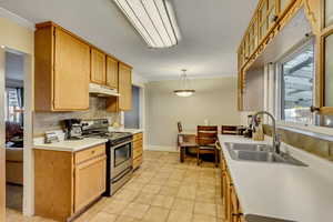 Kitchen with ornamental molding, light tile patterned floors, stainless steel electric range oven, hanging light fixtures, and sink