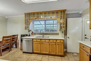 Kitchen featuring stainless steel dishwasher, sink, light tile patterned floors, and crown molding