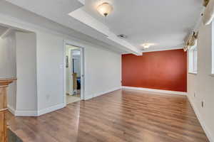 Empty room featuring wood-type flooring, ornamental molding, and a textured ceiling