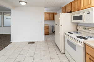 Kitchen with white appliances, a textured ceiling, and light tile patterned flooring