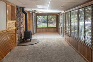 Unfurnished sunroom featuring a wood stove, a paneled ceiling, and ceiling fan