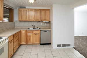 Kitchen featuring dishwasher, a textured ceiling, light carpet, sink, and backsplash