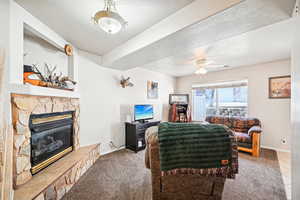 Carpeted living room featuring a stone fireplace, a textured ceiling, and ceiling fan