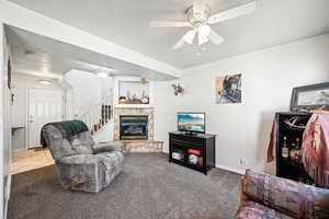 Carpeted living room featuring a fireplace, a textured ceiling, and ceiling fan