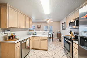 Kitchen featuring appliances with stainless steel finishes, a textured ceiling, light tile patterned floors, light brown cabinets, and kitchen peninsula