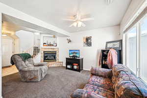 Carpeted living room featuring ceiling fan, a stone fireplace, and a textured ceiling