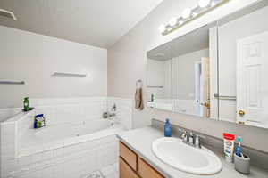 Bathroom with a textured ceiling, vanity, and tiled tub