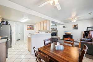 Dining area with a fireplace, light tile patterned flooring, ceiling fan, and a textured ceiling