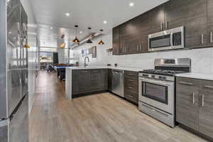 Kitchen with light wood-type flooring, appliances with stainless steel finishes, dark brown cabinetry, hanging light fixtures, and sink