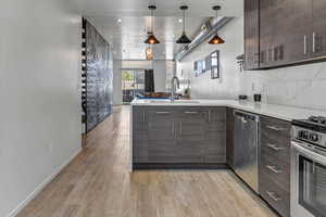 Kitchen with stainless steel appliances, sink, decorative light fixtures, dark brown cabinets, and light hardwood / wood-style flooring