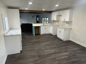 Kitchen featuring dark hardwood / wood-style flooring, kitchen peninsula, backsplash, light stone countertops, and white cabinetry