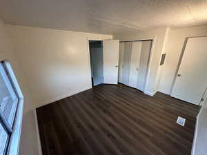 Unfurnished bedroom with dark wood-type flooring, a textured ceiling, and a closet