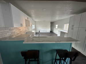 Kitchen featuring kitchen peninsula, decorative backsplash, sink, a breakfast bar, and white cabinetry