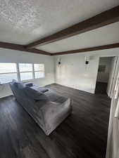 Living room featuring dark wood-type flooring, beamed ceiling, and a textured ceiling