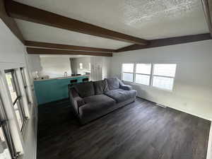 Living room with dark hardwood / wood-style floors, a textured ceiling, and lofted ceiling with beams