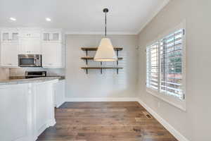 Kitchen with appliances with stainless steel finishes, decorative light fixtures, light stone countertops, white cabinets, and dark wood flooring