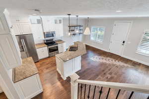 Kitchen featuring dark hardwood / wood-style flooring, white cabinetry, light stone counters, and appliances with stainless steel finishes