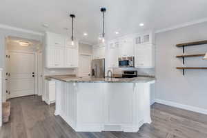 Kitchen with stainless steel appliances, light hardwood / wood-style floors, stone countertops, white cabinetry, and decorative light fixtures