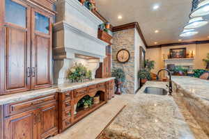 Clubhouse kitchen featuring a stone fireplace, hanging light fixtures, sink, ornamental molding, and light stone countertops