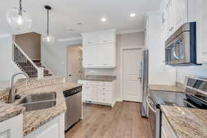 Kitchen featuring white cabinets, pendant lighting, light wood-type flooring, and appliances with stainless steel finishes