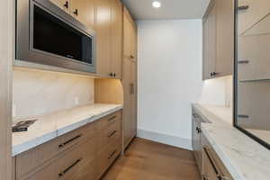 Kitchen featuring light stone counters, stainless steel microwave, tasteful backsplash, light hardwood / wood-style flooring, and light brown cabinetry