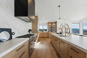 Kitchen with high end stainless steel range oven, hanging light fixtures, sink, wall chimney range hood, and light hardwood / wood-style flooring