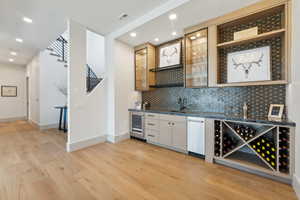 Bar with light hardwood / wood-style floors, white cabinetry, sink, and tasteful backsplash