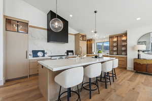 Kitchen featuring light wood-type flooring, decorative light fixtures, decorative backsplash, stainless steel range, and a spacious island