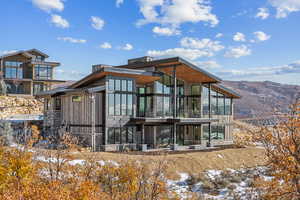 Snow covered rear of property featuring a sunroom, a mountain view, and a balcony