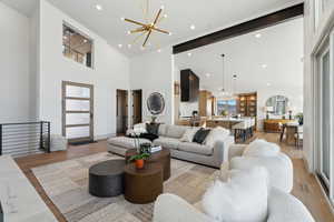 Living room with a high ceiling, beam ceiling, an inviting chandelier, and light hardwood / wood-style flooring