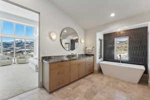 Bathroom featuring a tub to relax in, vanity, and lofted ceiling