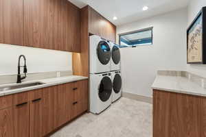 Laundry area with stacked washer / drying machine, cabinets, and sink