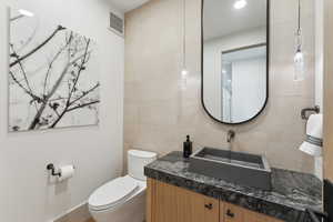 Bathroom featuring toilet, vanity, and tile walls