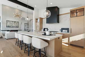 Kitchen with light hardwood / wood-style floors, hanging light fixtures, a center island with sink, and range hood