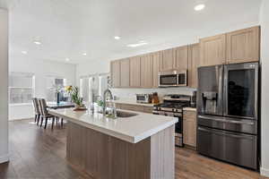 Kitchen featuring stainless steel appliances, sink, light brown cabinetry, an island with sink, and dark hardwood / wood-style flooring