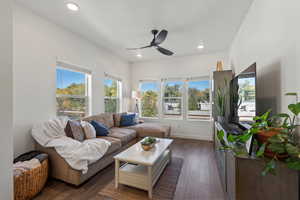 Living room with dark wood-type flooring, ceiling fan, and a healthy amount of sunlight