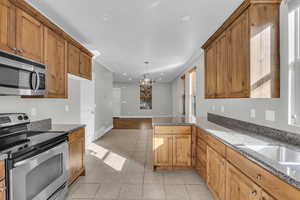 Kitchen with hanging light fixtures, dark stone countertops, kitchen peninsula, light tile patterned floors, and appliances with stainless steel finishes