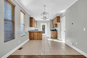 Kitchen with an inviting chandelier, appliances with stainless steel finishes, decorative light fixtures, light tile patterned floors, and ornamental molding