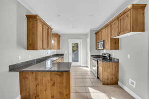 Kitchen with sink, kitchen peninsula, dark stone countertops, light tile patterned floors, and appliances with stainless steel finishes