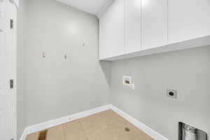 Clothes washing area featuring cabinets, hookup for a washing machine, light tile patterned floors, and electric dryer hookup