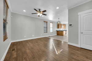 Unfurnished living room with wood-type flooring, ceiling fan, and ornamental molding