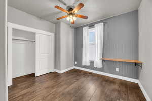 Unfurnished bedroom with a closet, dark hardwood / wood-style floors, ceiling fan, and wood walls