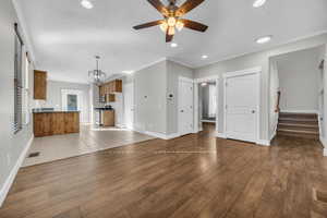 Unfurnished living room with ceiling fan with notable chandelier, light wood-type flooring, and ornamental molding