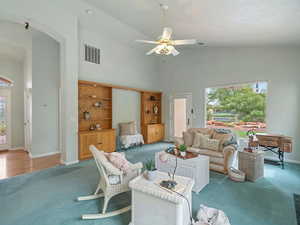 Carpeted living room with ceiling fan and high vaulted ceiling