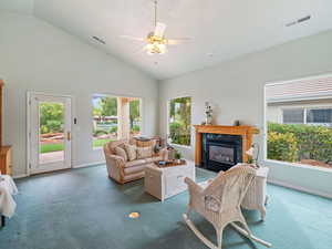 Carpeted living room with a premium fireplace, ceiling fan, high vaulted ceiling, and a healthy amount of sunlight