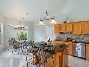 Kitchen featuring sink, tasteful backsplash, decorative light fixtures, stainless steel dishwasher, and a center island